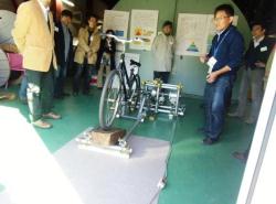 フライホイール型直流発生装置の原理を、自転車を用いたモデルを用いて説明する金道浩一教授