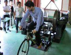 フライホイール型直流発生装置の原理を自転車を用いたモデルを用いて説明する金道教授