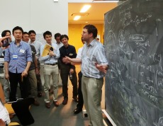 数式で埋め尽くされたIPMUの黒板の前で説明するワーナー特任研究員